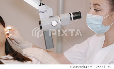 Doctor examining the ear of a young woman in clinic Doctor examining the ear of a young woman in clinic 75361030