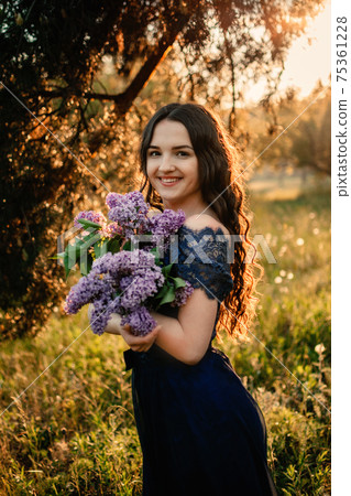 Party graduation prom fairytale concept. Beautiful brunette young woman in blue prom dress with lilac bouquet on nature background. Outdoor romantic portrait of brunette girl in long evening dress Party graduation prom fairytale concept. Beautiful brunette young woman in blue prom dress with lilac bouquet on nature background. Outdoor romantic portrait of brunette girl in long evening dress 75361228