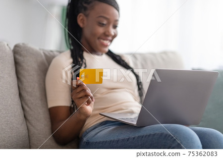 Closeup of positive black woman holding credit card, using laptop 75362083