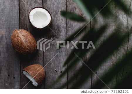 Broken coconuts on gray wooden background with palm leaf. White coconut pulp 75362191