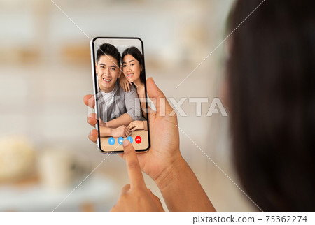 Remote communication concept. Young lady talking to happy Asian couple online on cellphone, chatting on web with friends Remote communication concept. Young lady talking to happy Asian couple online on cellphone, chatting on web with friends 75362274