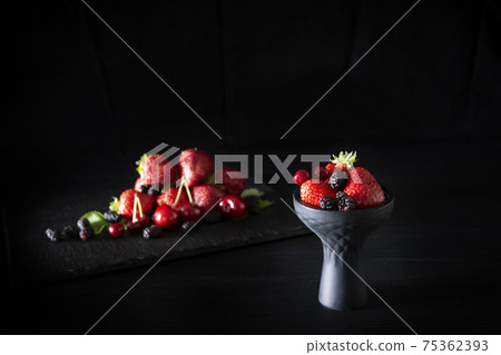 Hookah bowl with berries on blured dark fruits on dark wood table. Hookah bowl with berries on blured dark fruits on dark wood table. 75362393