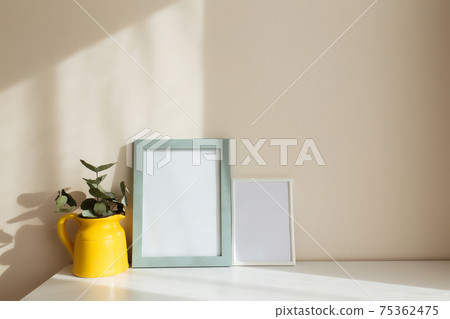 Yellow ceramic jug or vase with eucalyptus branches, empty white photo frames Yellow ceramic jug or vase with eucalyptus branches, empty white photo frames 75362475