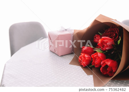 Bouquet of red tulips on table and pink gift box. Concept for greeting card Bouquet of red tulips on table and pink gift box. Concept for greeting card 75362482