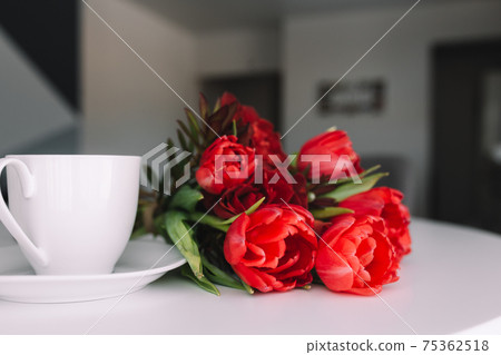 Bouquet of red tulips on table and white coffee cup. Concept for greeting card Bouquet of red tulips on table and white coffee cup. Concept for greeting card 75362518
