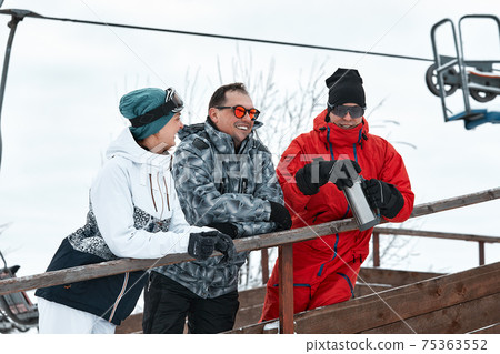 group of skiers friends on the mountain are resting and drinking coffee from a thermos on the background of the ski lift group of skiers friends on the mountain are resting and drinking coffee from a thermos on the background of the ski lift 75363552