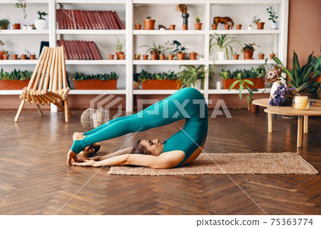 Young sporty woman practicing yoga at home doing exercise Halasana Plow Pose Young sporty woman practicing yoga at home doing exercise Halasana Plow Pose 75363774