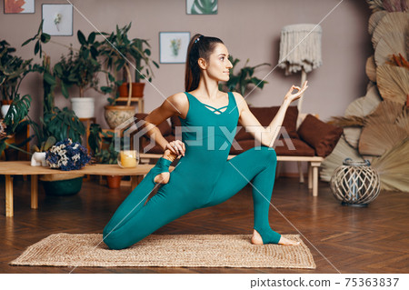 Young sporty woman practicing yoga at home doing Eka Pada Rajakapotasana, One legged king pigeon variation 75363837