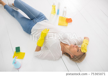 Tired housewife in yellow gloves laying on the floor 75365871