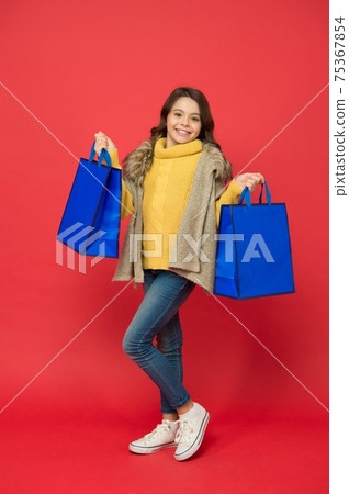 Happy little girl with fashion look carry shopping bags red background, sale 75367854