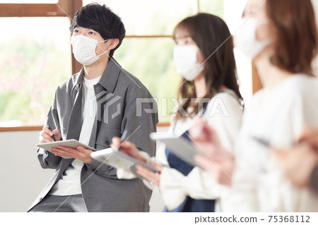 A young man wearing a mask taking notes on a tablet A young man wearing a mask taking notes on a tablet 75368112
