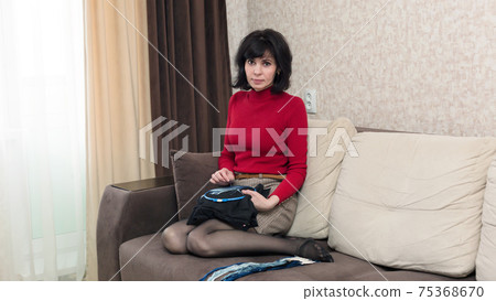 Woman in red clothes sitting on the couch is embroidering a picture in a cross 75368670