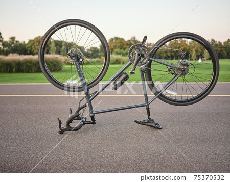 Broken bike. Malfunctioning upside down road bicycle parked for repairing in public park on a daytime Broken bike. Malfunctioning upside down road bicycle parked for repairing in public park on a daytime 75370532