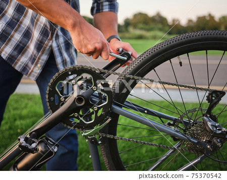 Close up shot of hands of man fixing pedals on his bike, standing in public park 75370542