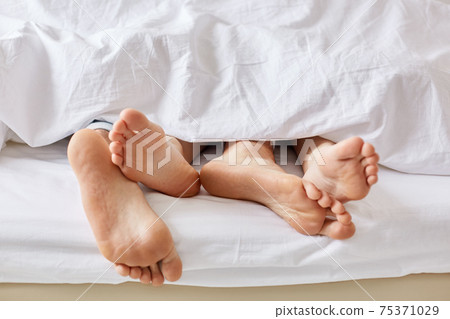 Lazy day concept. Wifes and husbands bare feet from white blanket. Female and male stay in bed, focus on legs, enjoy weekend and togetherness, sleep for long time. People, rest and relax concept Lazy day concept. Wifes and husbands bare feet from white blanket. Female and male stay in bed, focus on legs, enjoy weekend and togetherness, sleep for long time. People, rest and relax concept 75371029