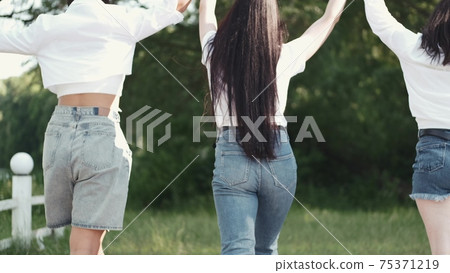 Three pretty brunette girlfriends going on the grass holding hands Three pretty brunette girlfriends going on the grass holding hands 75371219