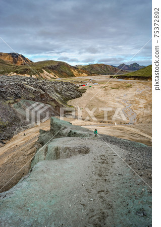 Beautiful Icelandic landscape of colorful rainbow volcanic Landmannalaugar mountains, at famous Laugavegur hiking trail with dramatic snowy sky and hikers at distance in Iceland. 75372892