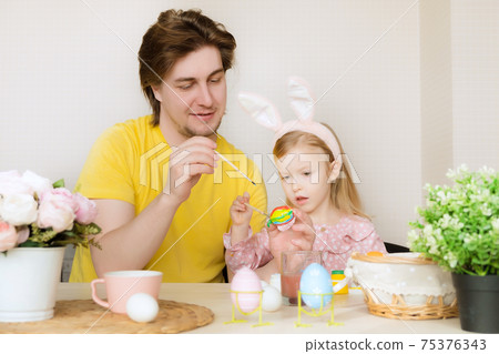 Easter, family, holiday and children concept. Father and daughter painting eggs. Happy family preparing for Easter 75376343