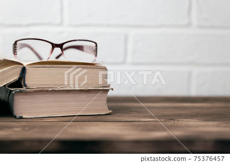 Offline education concept reading learning erudition, poor eyesight, open book and glasses on a wooden table against a white brick wall background with copy space Offline education concept reading learning erudition, poor eyesight, open book and glasses on a wooden table against a white brick wall background with copy space 75376457