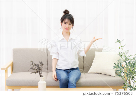 A young woman sitting on the sofa in the room and making a guiding gesture A young woman sitting on the sofa in the room and making a guiding gesture 75376503