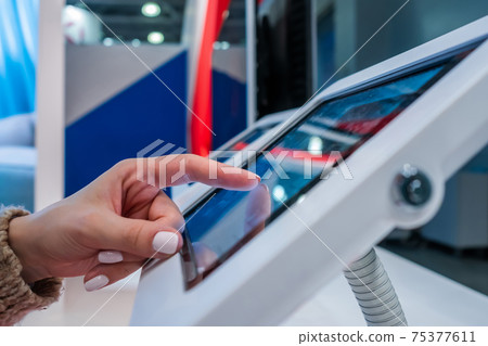 Woman hand using touchscreen display of floor standing white tablet kiosk Woman hand using touchscreen display of floor standing white tablet kiosk 75377611