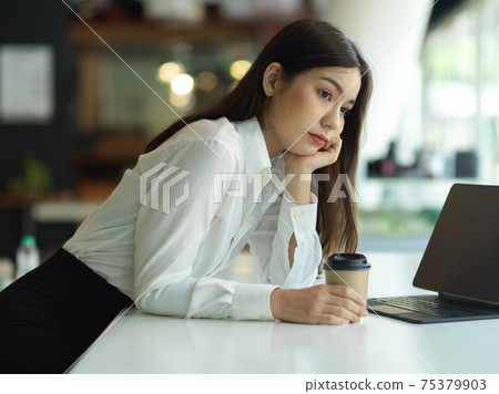 Female worker holding paper cup while thinking about her work 75379903