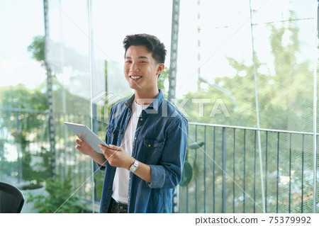 Portrait of a young confident smiling indian man holding a tablet and looking into the distance Portrait of a young confident smiling indian man holding a tablet and looking into the distance 75379992
