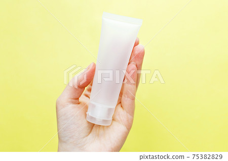 Female hand holding cream tube cosmetic products on yellow background 75382829