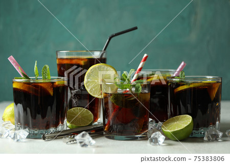 Glass of Cuba Libre on white textured table against blurred lights 75383806