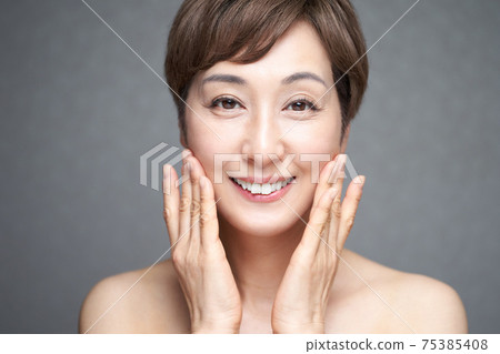 A middle-aged Japanese woman checking the moisture of her cheeks with both hands 75385408
