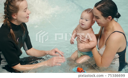Mother and infant son at swimming lesson with female instructor Mother and infant son at swimming lesson with female instructor 75386699
