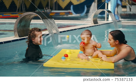 Mother and infant son at swimming lesson with female instructor 75387133