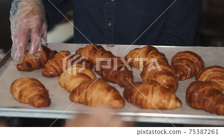 Woman in gloves checks freshly baked croissants on a tray Woman in gloves checks freshly baked croissants on a tray 75387261