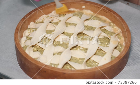 Chef at industrial kitchen decorating spinach pie with dough stripes Chef at industrial kitchen decorating spinach pie with dough stripes 75387266