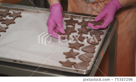 Woman is putting gingerbread cookies on baking tray Woman is putting gingerbread cookies on baking tray 75387296