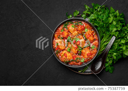 Chicken Vindaloo with spinach in black bowl on dark slate table top. Indian cuisine meat curry dish 75387739