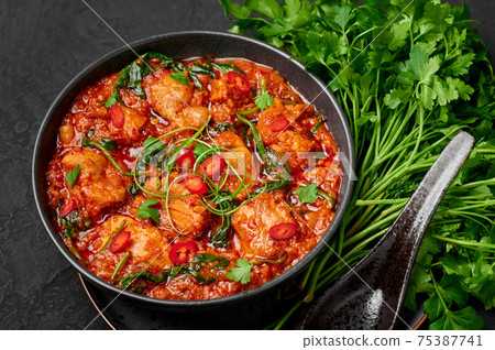 Chicken Vindaloo with spinach in black bowl on dark slate table top. Indian cuisine meat curry dish 75387741