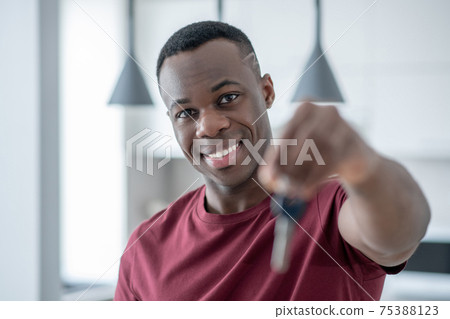 Smiling african american guy holding the key and stretching his hand Smiling african american guy holding the key and stretching his hand 75388123