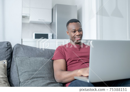 A dark-skinned young man working from home and looking involved A dark-skinned young man working from home and looking involved 75388151