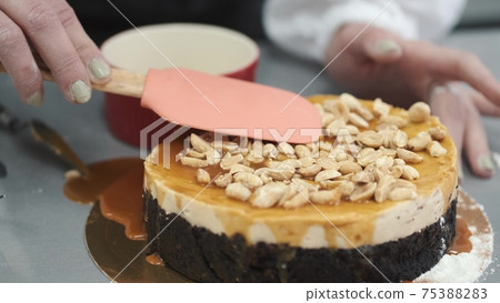 Female pastry chef prepares a cake and decorates it with cashew Female pastry chef prepares a cake and decorates it with cashew 75388283