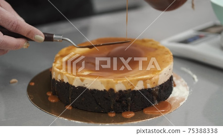 Female chef is working on cake, standing at table in kitchen Female chef is working on cake, standing at table in kitchen 75388338
