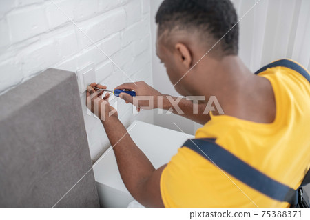 Dark-skinned service man in yellow tshirt working with screwdriver Dark-skinned service man in yellow tshirt working with screwdriver 75388371