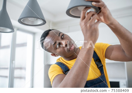 Dark-skinned service man in yellow tshirt repairing electricity lamps 75388409