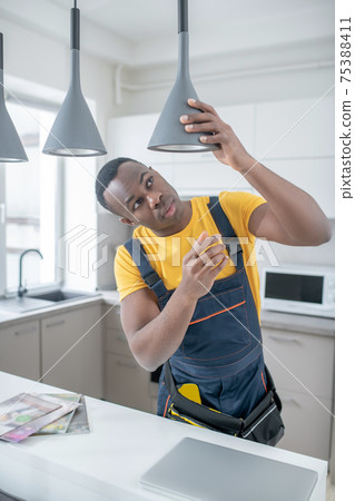 Dark-skinned service man in yellow tshirt repairing electricity lamps 75388411