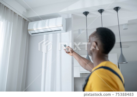 Dark-skinned service man in yellow tshirt installing the air-conditioner Dark-skinned service man in yellow tshirt installing the air-conditioner 75388483