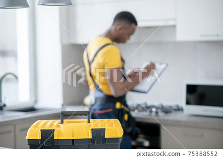 Dark-skinned service man standing in the kitchen and making notes Dark-skinned service man standing in the kitchen and making notes 75388552