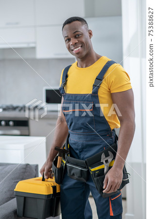 Dark-skinned service man standing in the kitchen and holding a box with tools Dark-skinned service man standing in the kitchen and holding a box with tools 75388627