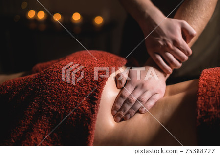 Massage of a female back in a dark room of a spa salon. Male masseur doing massage of the back of the body and lower back 75388727