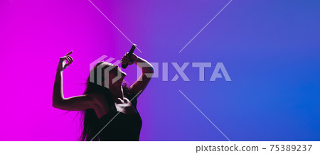 Portrait of young female singer isolated on blue-pink background. 75389237