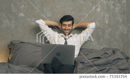 Happy business middle east man person watching a funny movie online and laughing on bed in bedroom at home at late night. Activity lifestyle. Relax time. Computer notebook laptop in technology device. 75393704